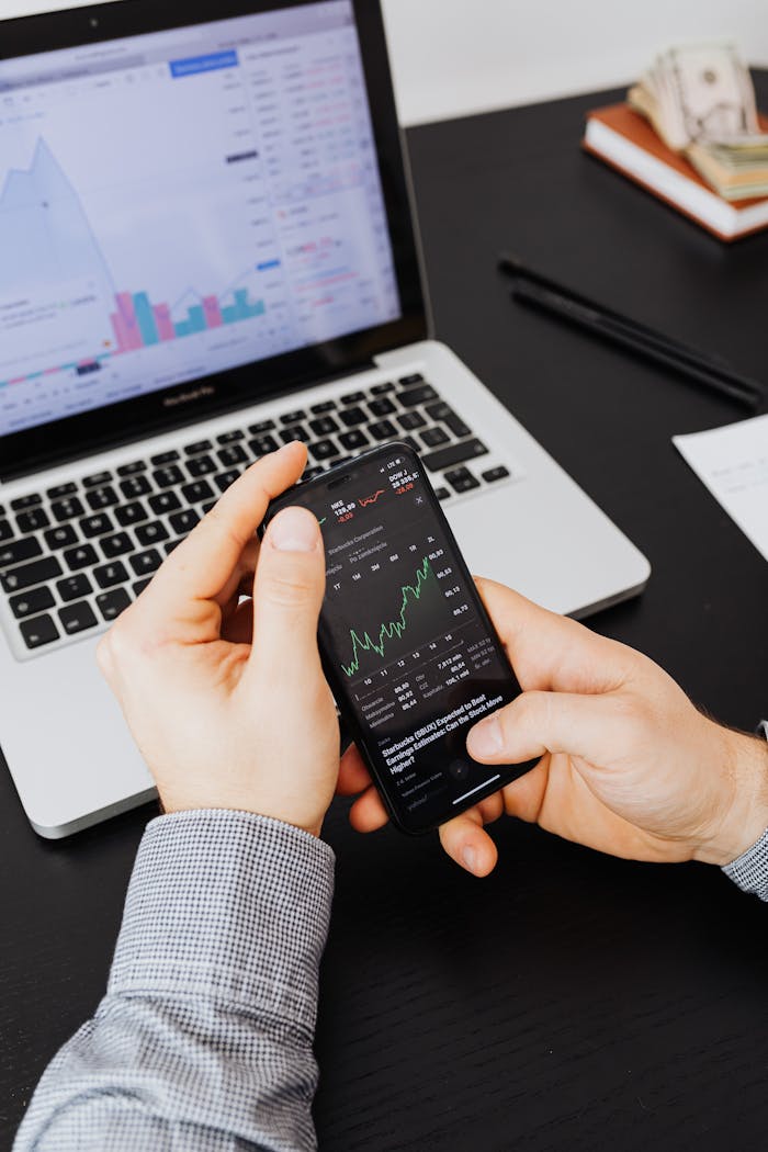Close-up of hands examining stock market graphs on smartphone and laptop.
