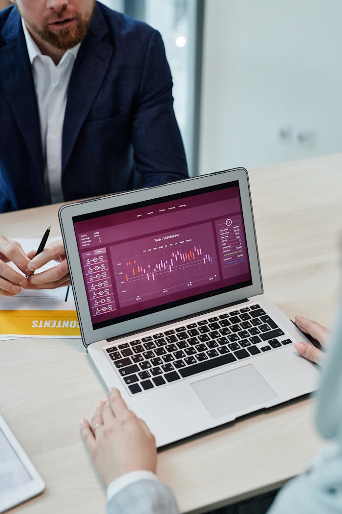 High-angle shot of business meeting with graph on laptop screen and documents on table.